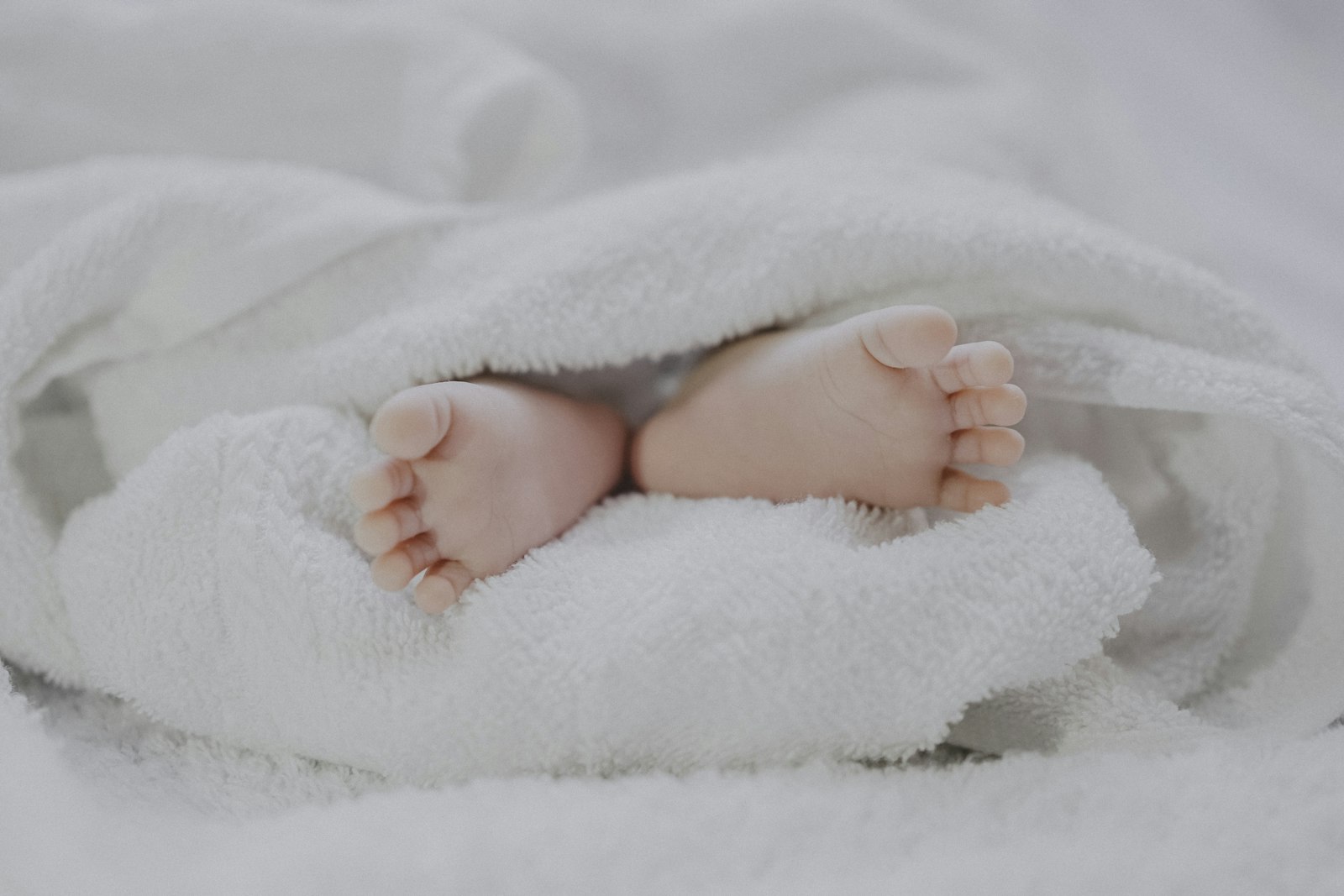 A newborn baby's feet peeking out from a soft white blanket