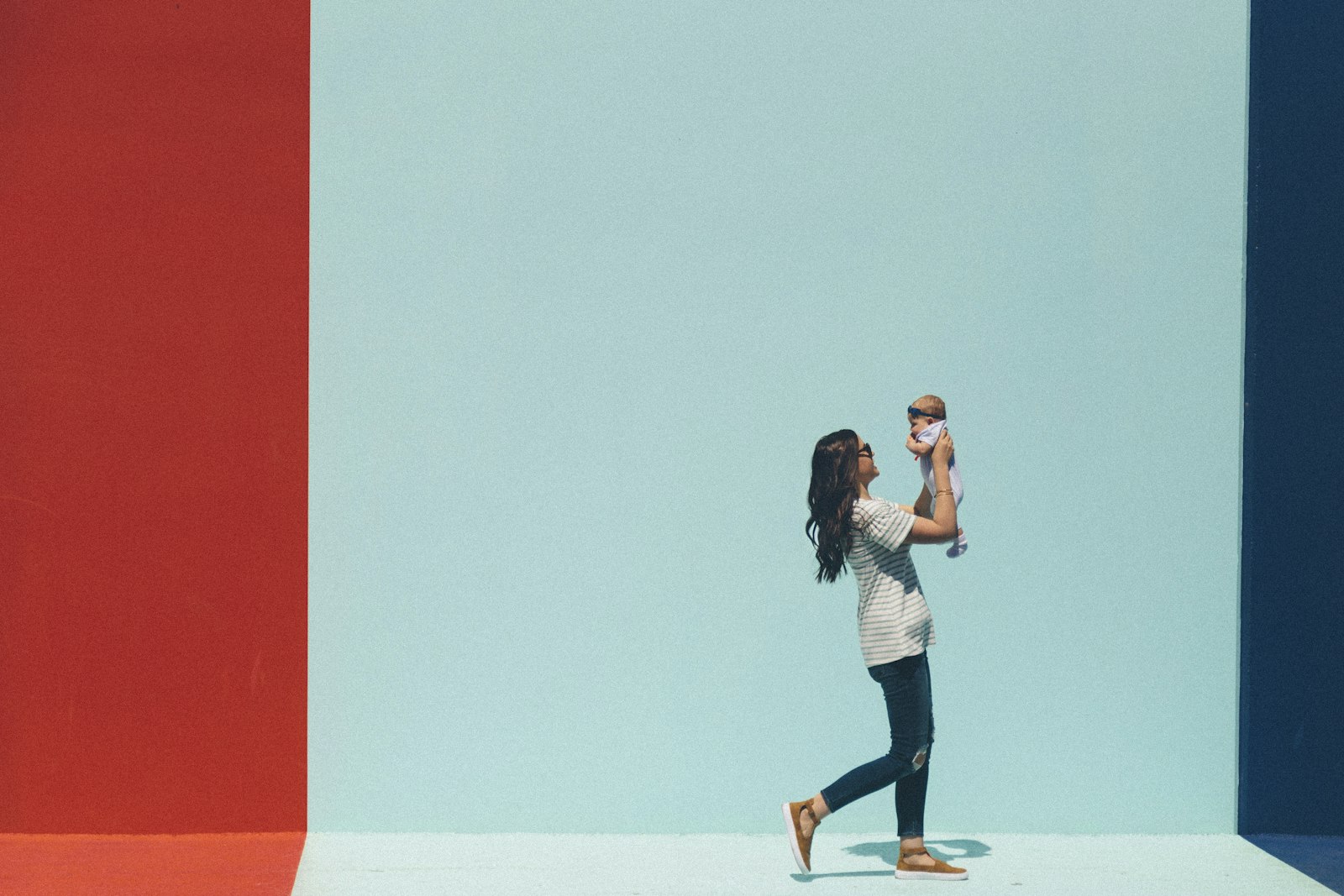 A parent lifting a laughing baby overhead against a bright, minimal wall